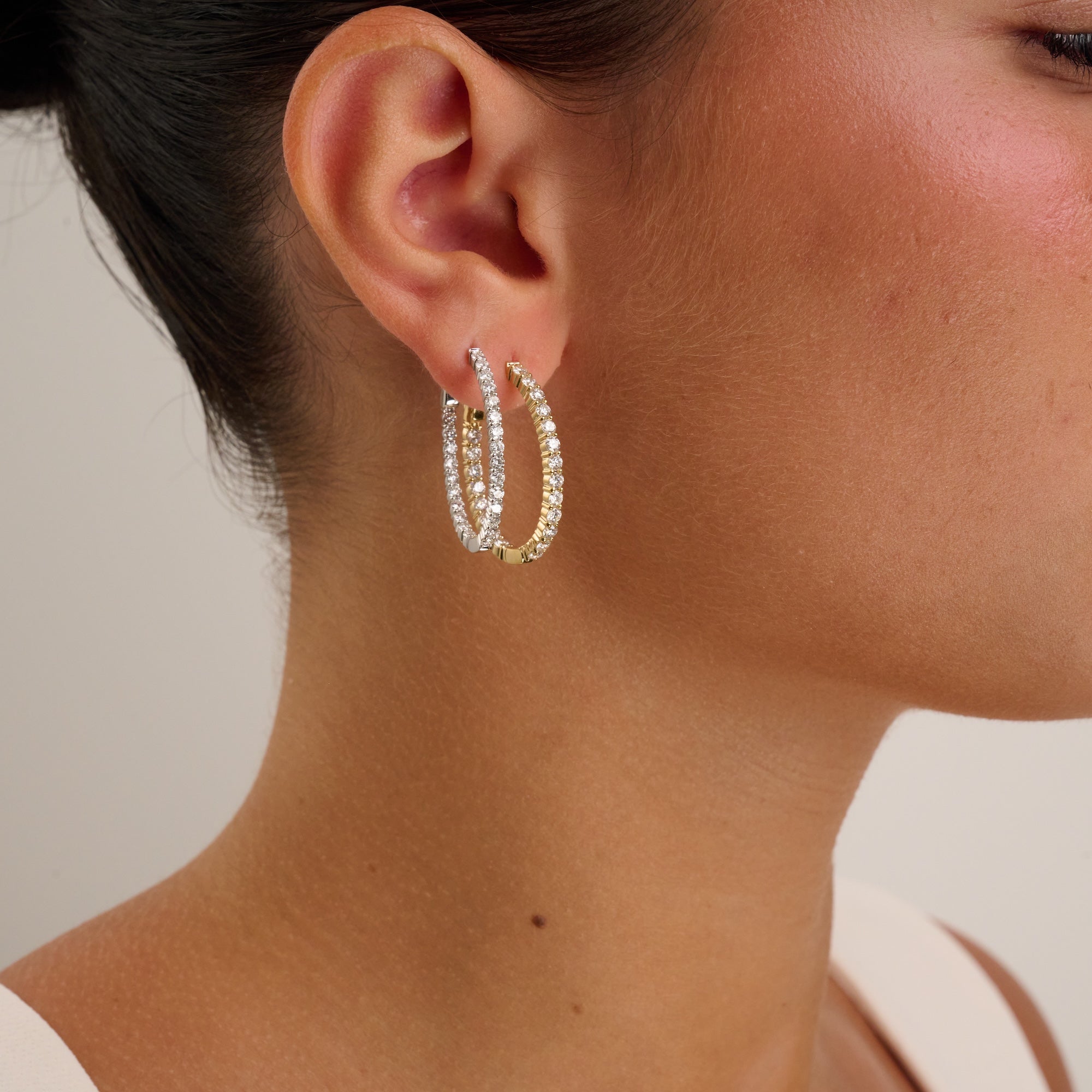 Close-up of a person wearing gold hoop earrings with a neutral background